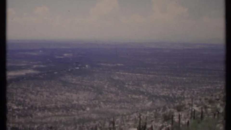 1971 California 8mm frame of a broad desert panorama, with sparse vegetation in front and hazy distance beyond.