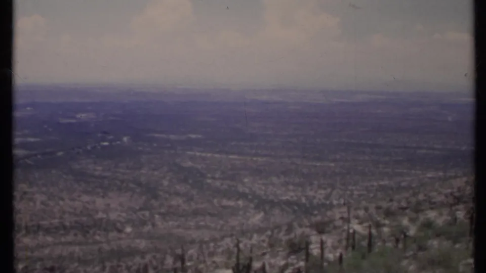 1971 California 8mm frame showing an arid valley from above, with brushy foreground plants and a faded hazy sky.