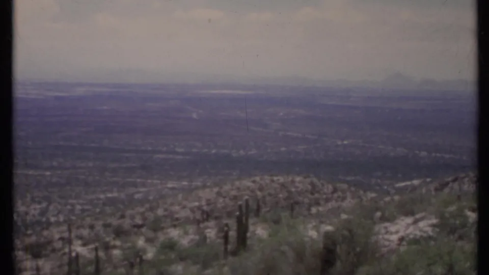 1971 California 8mm frame with tall cactus forms on a rocky hillside and a muted valley stretching toward distant ridges.