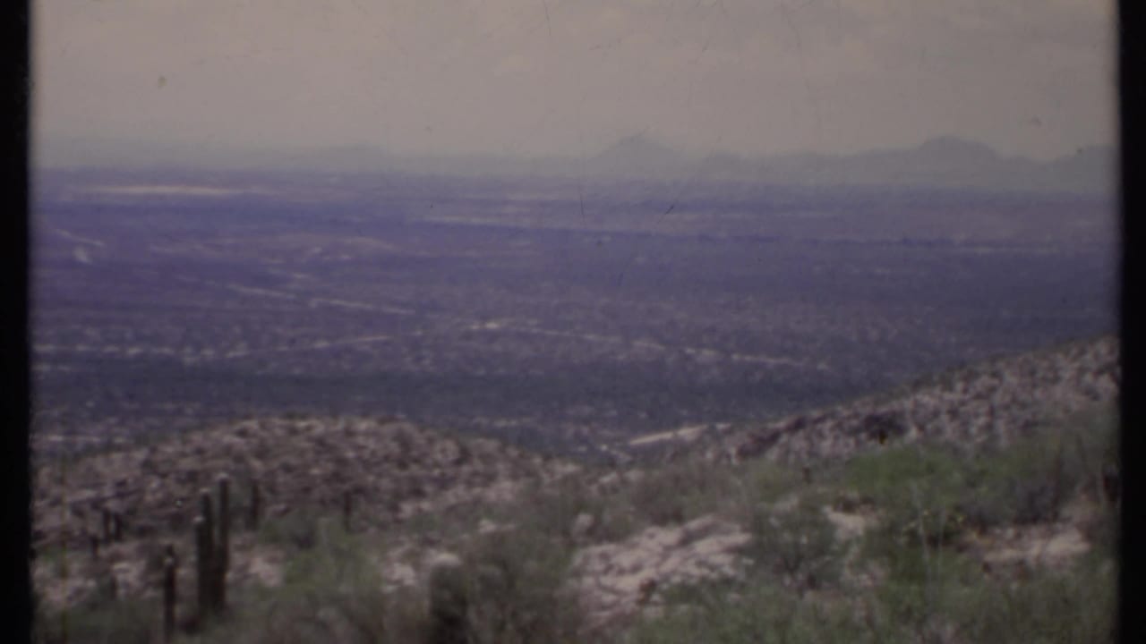 Rocky desert hillside with cactus overlooking a hazy valley and distant mountains.