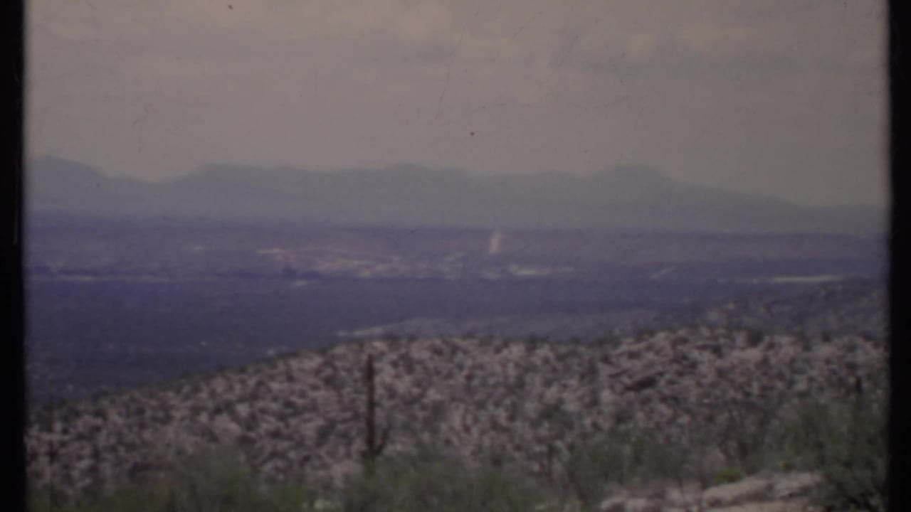 Hazy desert valley with scrub foreground and distant mountain ridges.