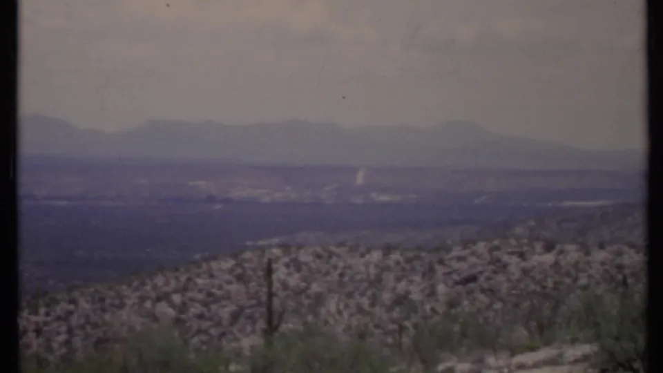 1971 California 8mm view of a hazy desert valley, low scrub, and soft distant mountain ridges under a pale sky.
