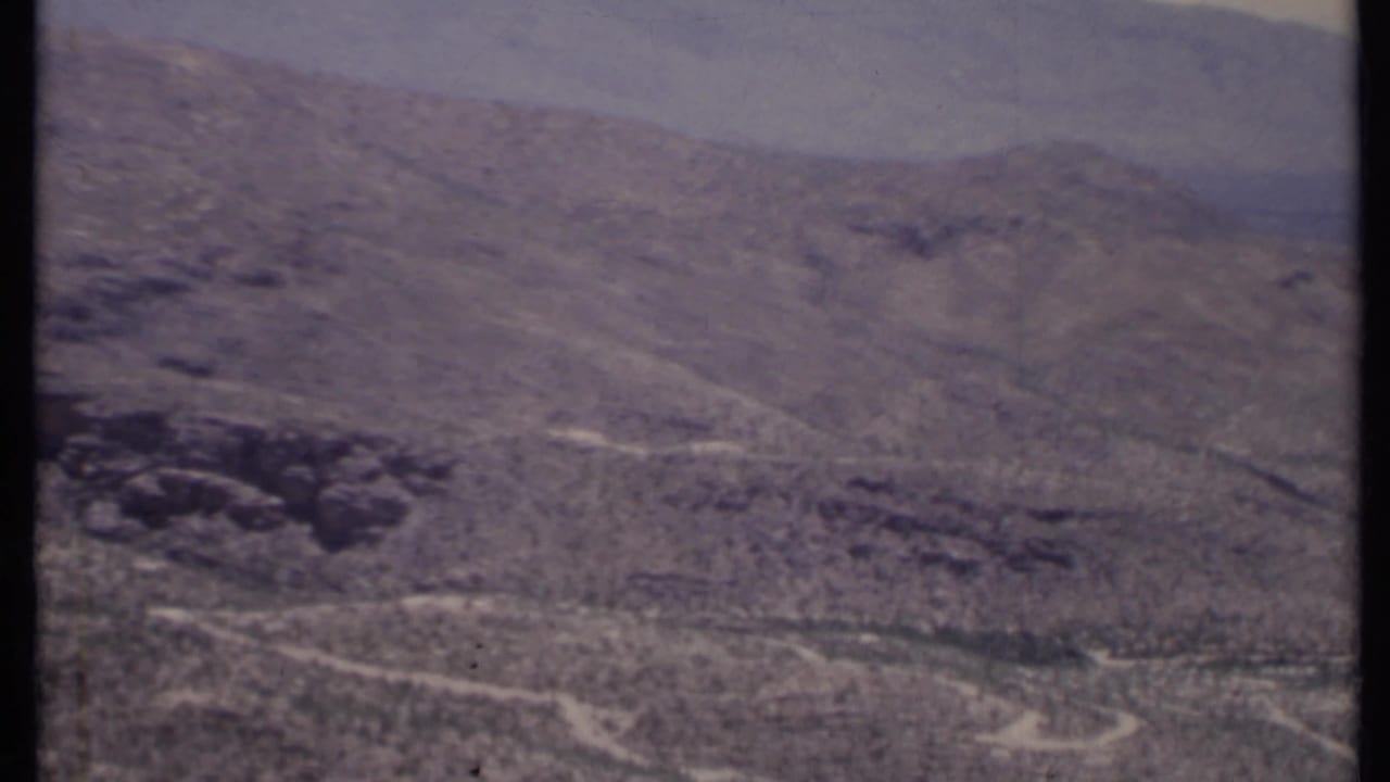 Aerial view of arid hills with sparse shrubs and pale dirt tracks.