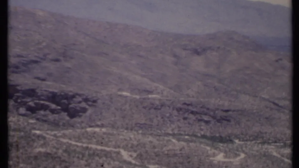 1971 California 8mm aerial view of dry, shrub-dotted hills with winding dirt trails under a hazy sky.
