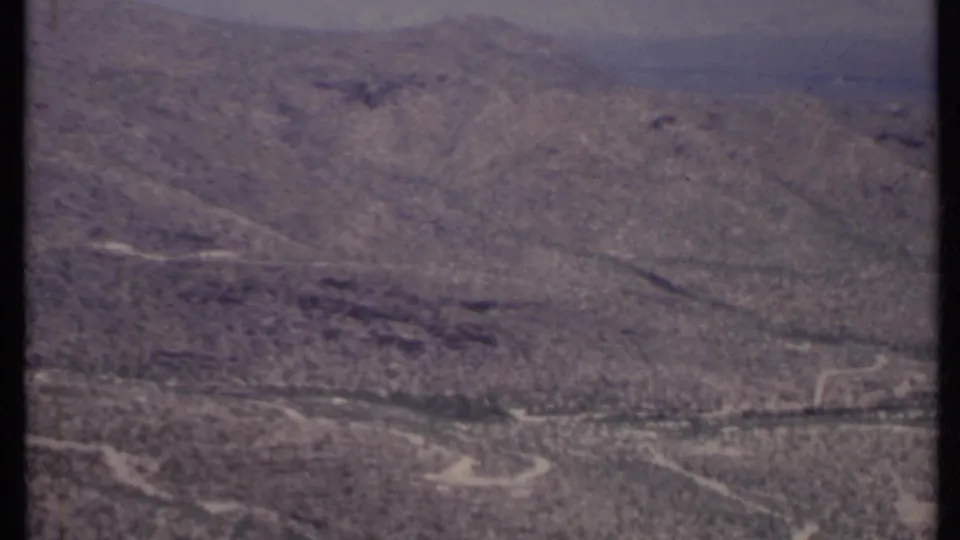 1971 California aerial home-movie frame showing broad arid terrain, faint roads, and scattered desert vegetation.