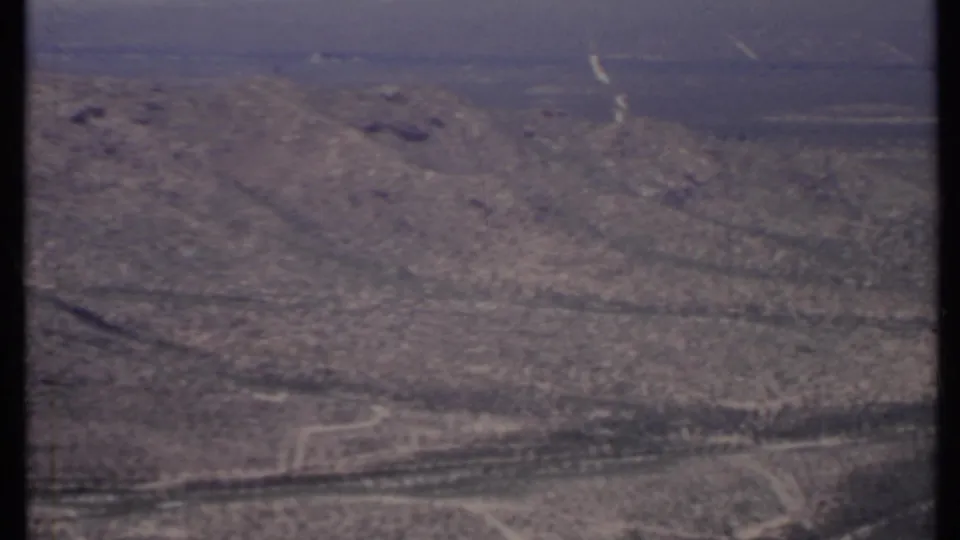1971 California aerial view of rugged desert land, scattered shrubs, and a curving dirt road crossing the lower frame.