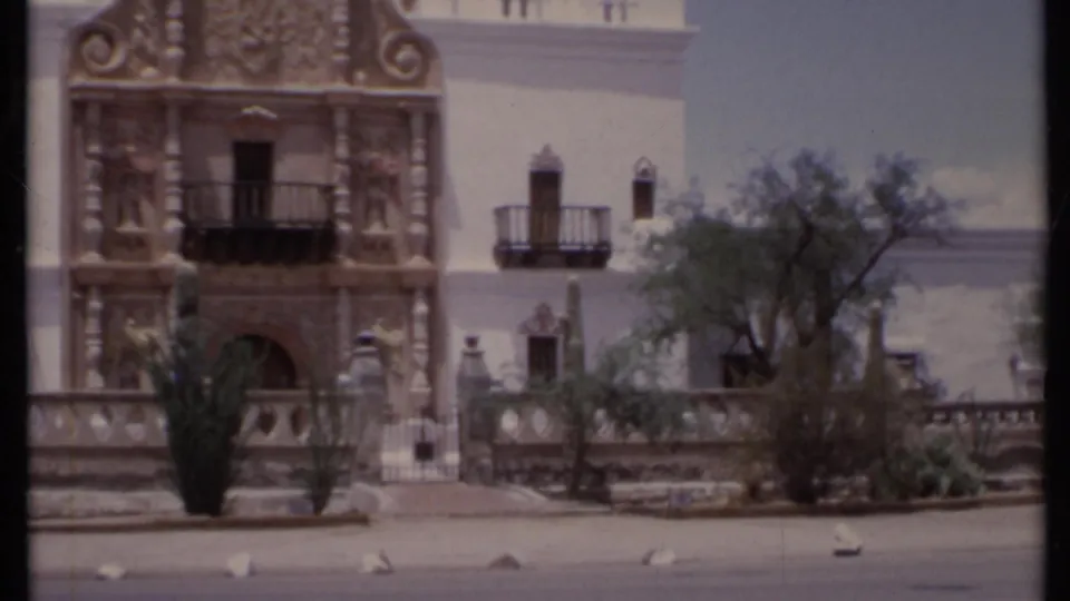 1971 California 8mm frame centered on an ornate Spanish-style entrance with carved details, arched doorway, balcony and desert landscaping.