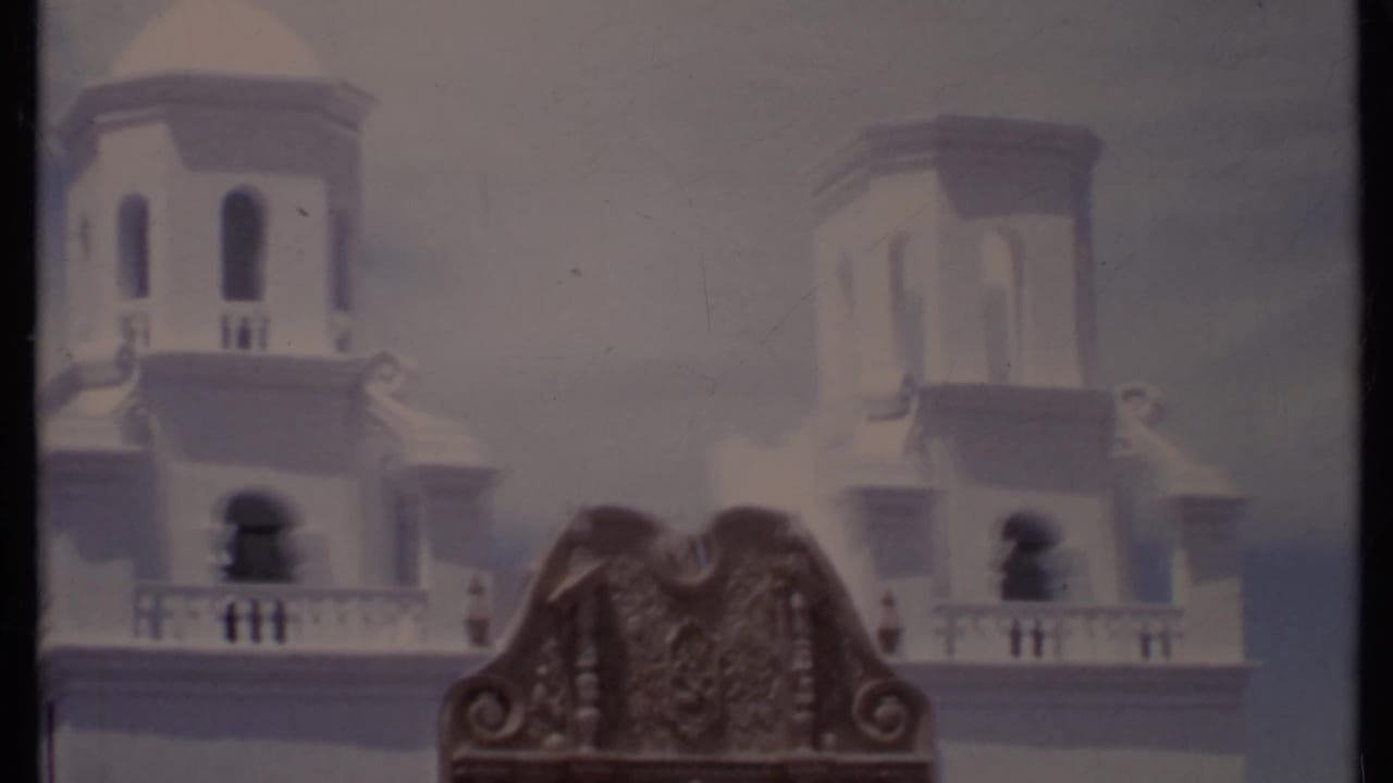 White towered building facade with arched openings and ornate wooden detail in front.