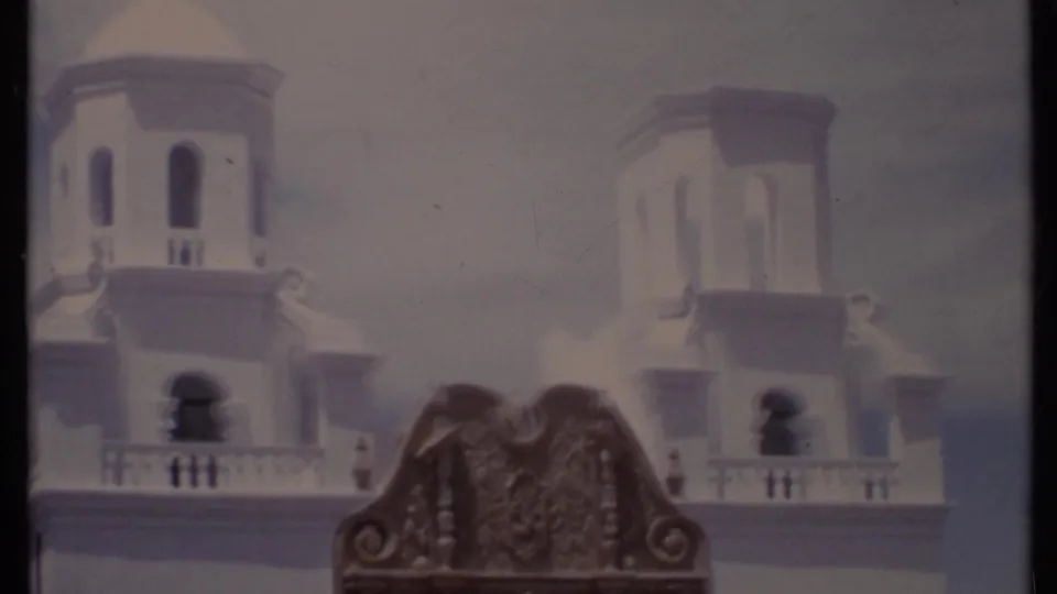 1971 California 8mm frame showing a white colonial-style building with tower openings, balcony railings, and a carved wooden foreground detail.