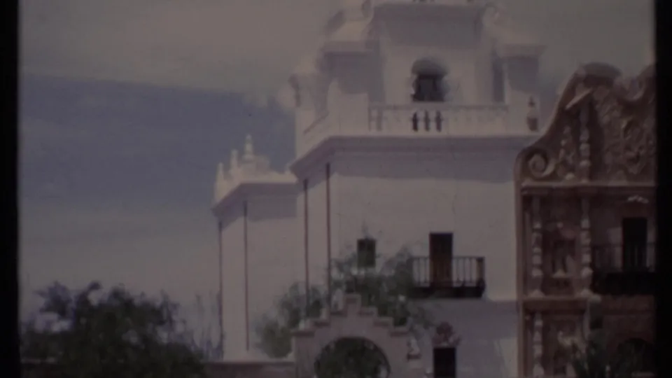 1971 California 8mm frame showing the building from the side, with a balcony, arched lower opening, ornamental trim, trees, and clouded sky.