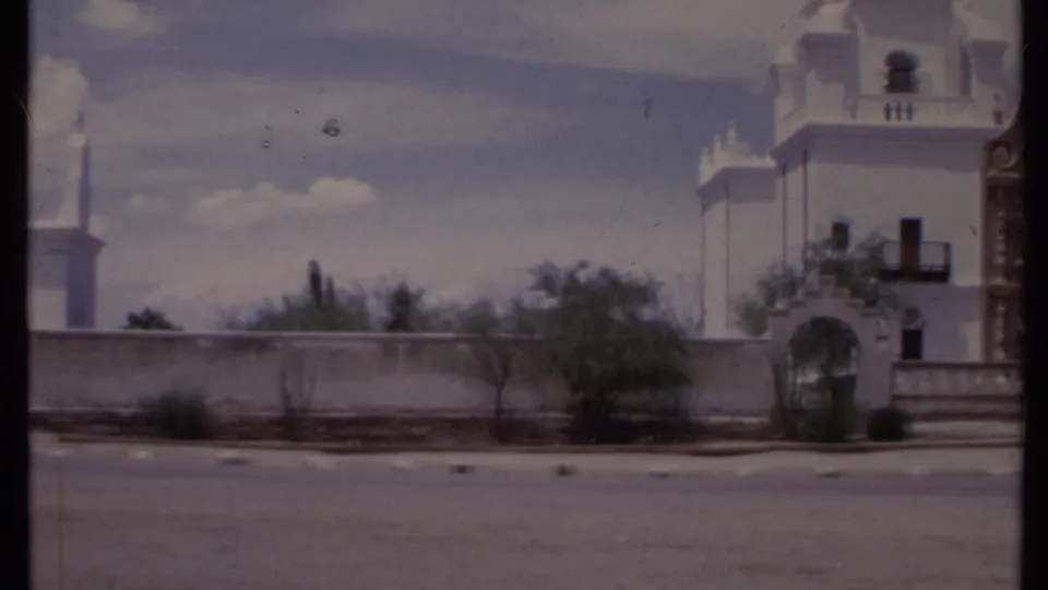 1971 California 8mm frame showing the arched gateway and towered white building beyond a paved parking area.