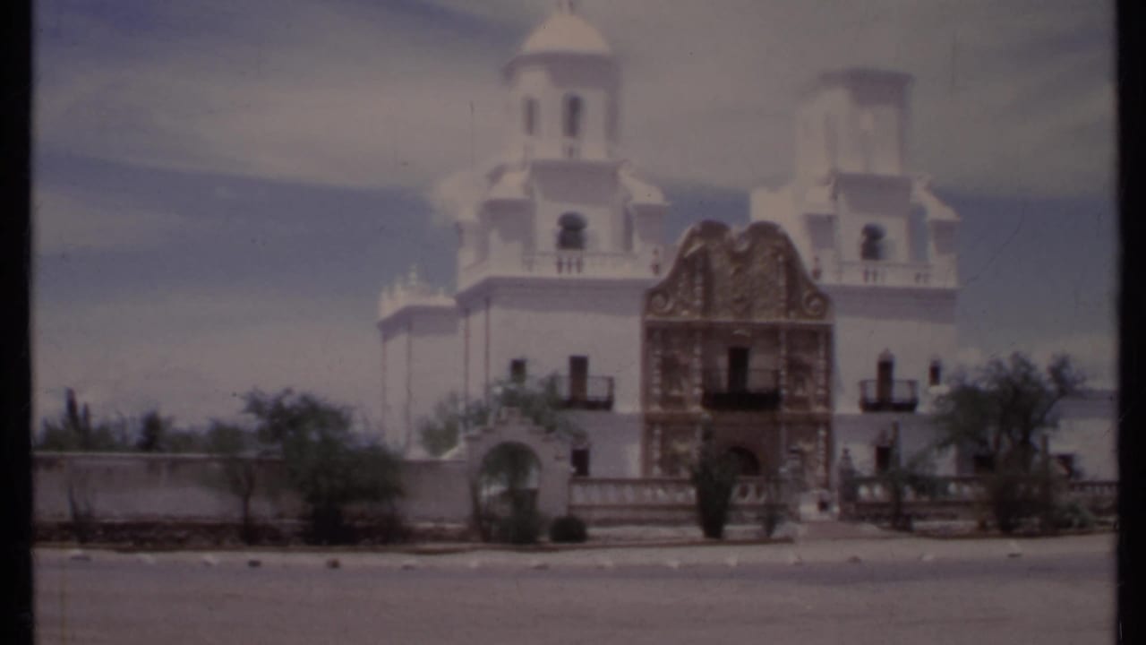 White mission-style building with brown ornate facade and twin towers across a street.