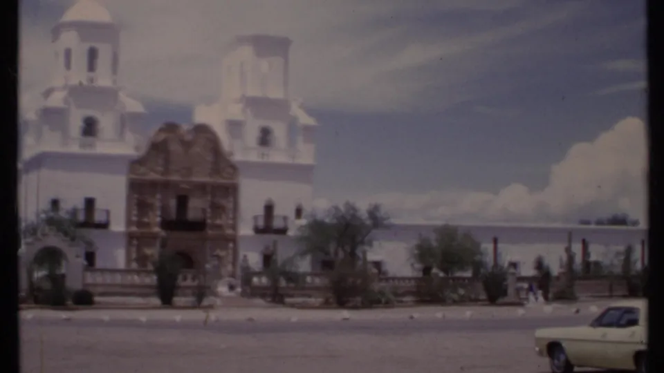 1971 California 8mm frame with the white towers, ornate brown entrance, small visitors near the wall, and a pale car entering frame.