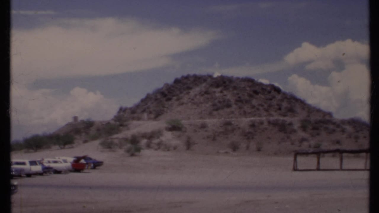 Wide 8mm view of a rocky desert hill with parked cars in the foreground.