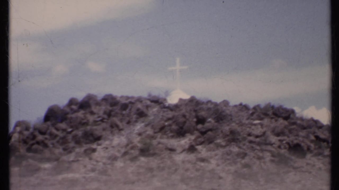 Rocky hillside with a white cross under a cloudy sky.