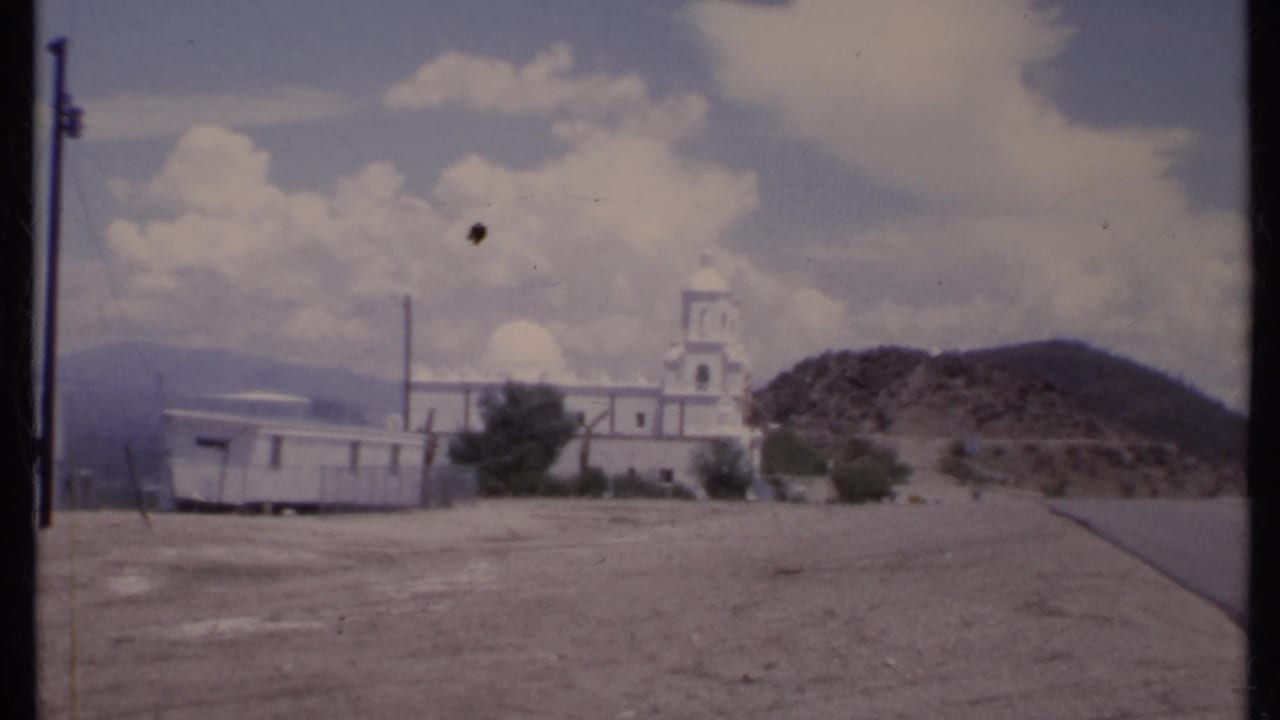 White church, mobile home, utility poles, and hillside under clouds.