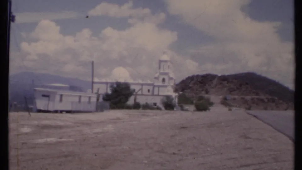 1971 California 8mm frame showing a white church, mobile home, utility pole, hillside, and distant mountains.