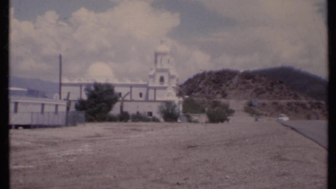 White church beside a desert road with a rocky hill behind it.