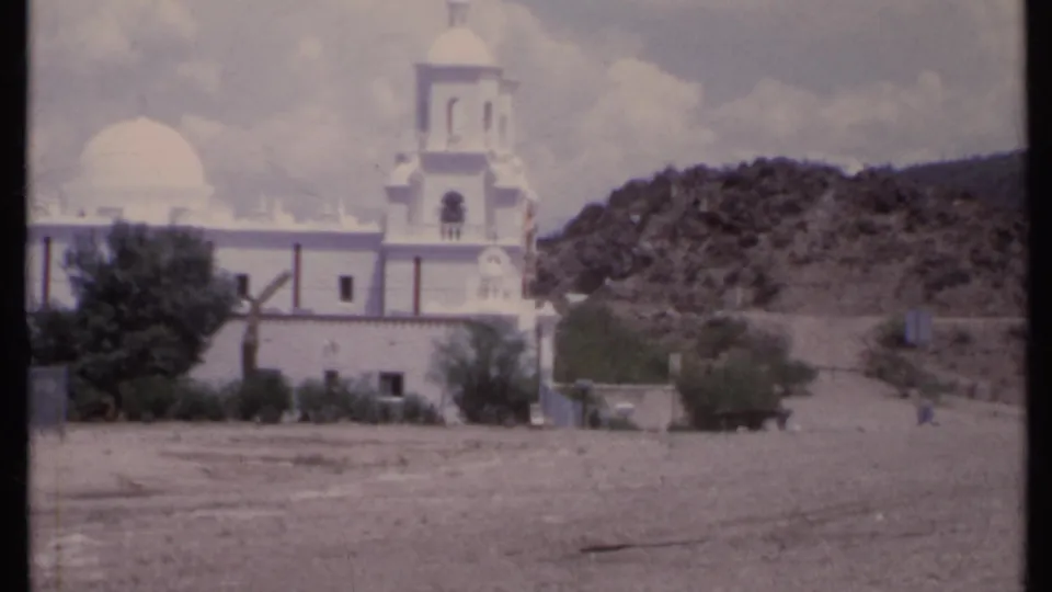 1971 California 8mm frame showing a white church with dome and bell tower against a dry rocky hillside.