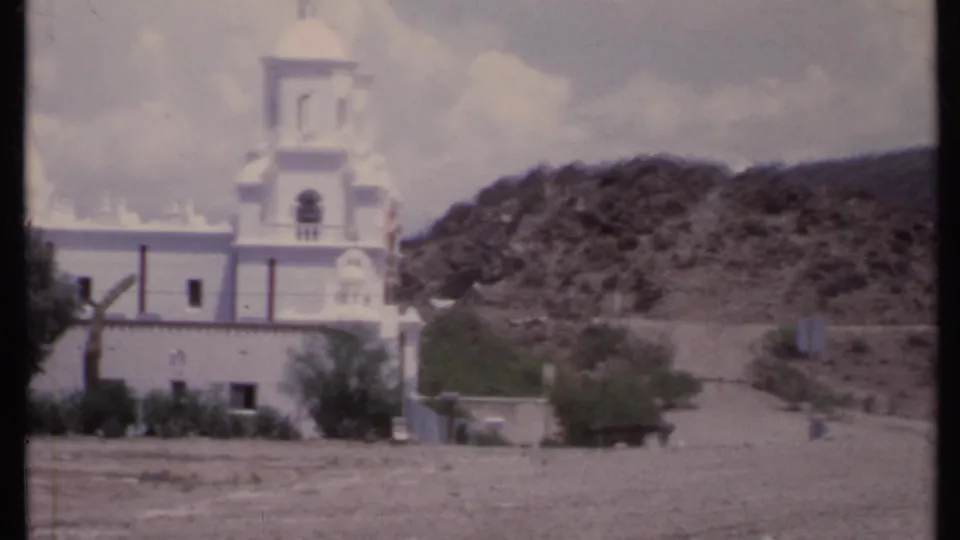 1971 California 8mm frame with the church facade, bell tower, dome edge, hillside, and road area visible during the zoom.