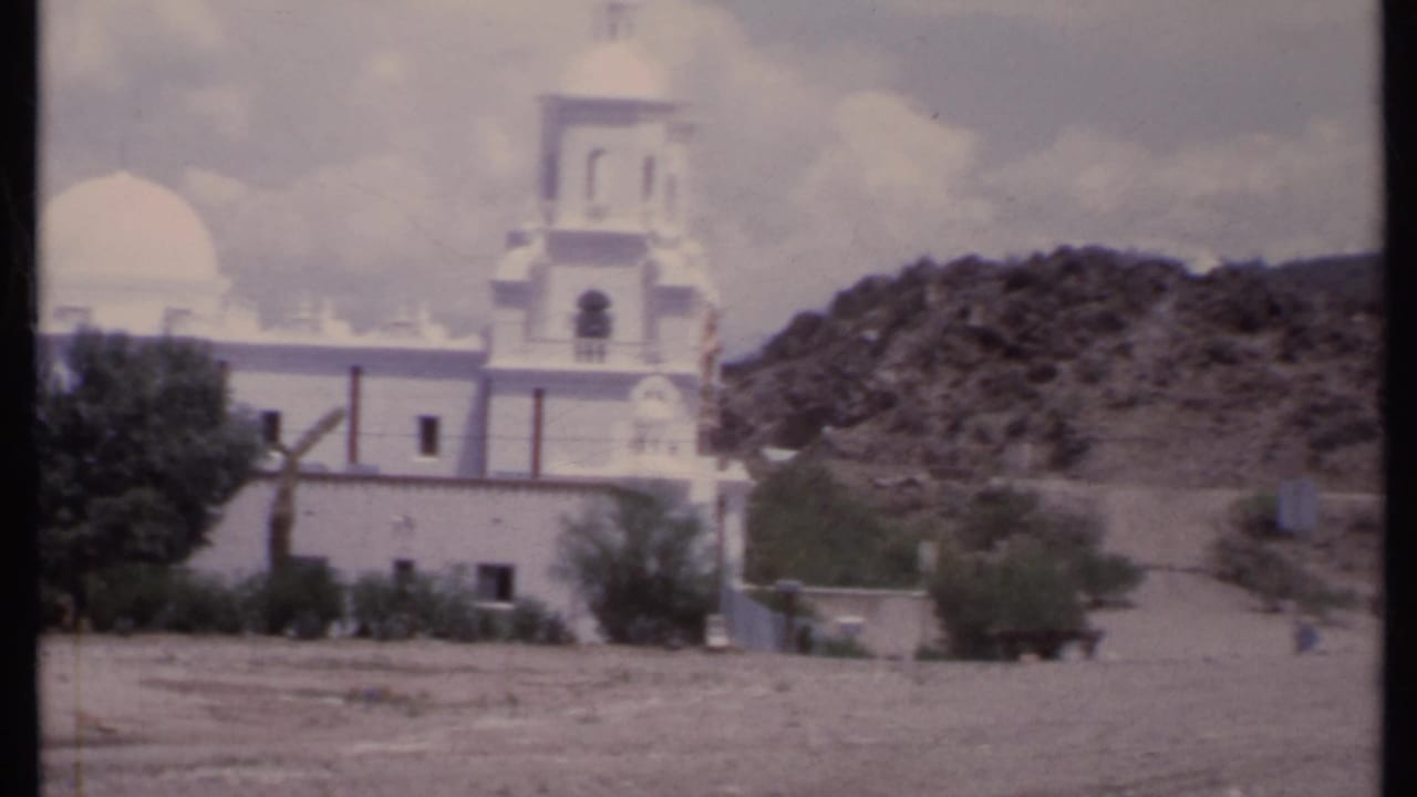White church with dome and bell tower beside a dry hillside.