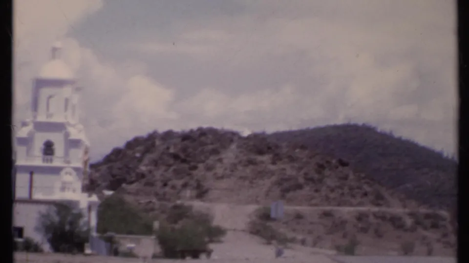 1971 California 8mm frame with the church partly cropped at left and a scrub-covered hill filling the background.