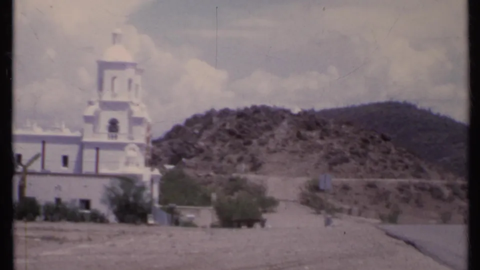 1971 California 8mm frame showing the church tower and dome partially cropped, with arid ground and a mountain backdrop.