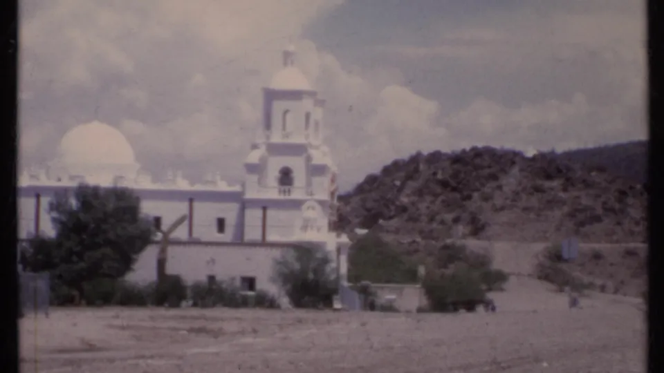 1971 California 8mm frame with the white church, dome, and bell tower framed against dry foothills and open sky.