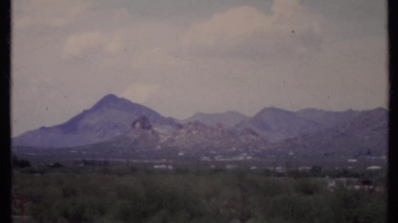 Hazy desert mountains beyond low scrub and a dark 8mm frame edge.