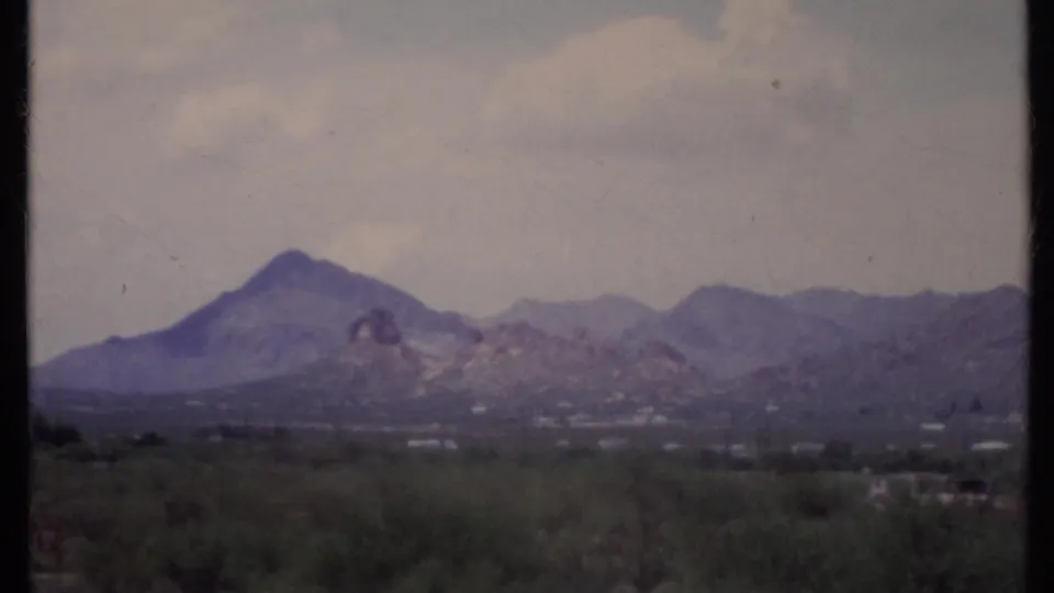 1971 California 8mm frame showing distant desert mountains under a pale sky, with scrub in the foreground and film gate edges visible.