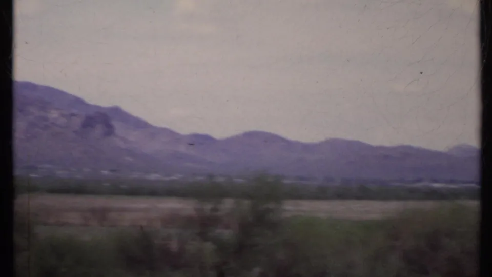 1971 California home-movie view of a low mountain range across open desert, with motion-softened foreground brush and faded 8mm color.
