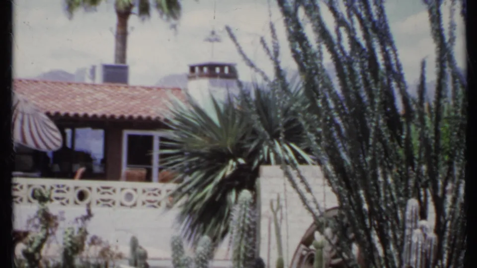 1971 California home exterior with terracotta tile roof, palm, desert plants, and a patterned white wall in soft 8mm color.