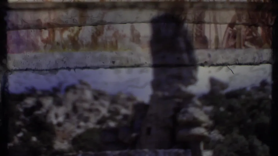 Faded 1971 8mm view of a cactus and stone wall with rocky hillside and shrubs, partially obscured by film-frame shadow.