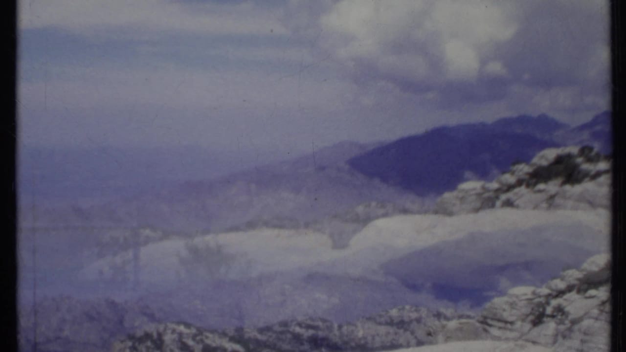 Mountain ridges under a blue sky with large white clouds and rocky foreground slopes.