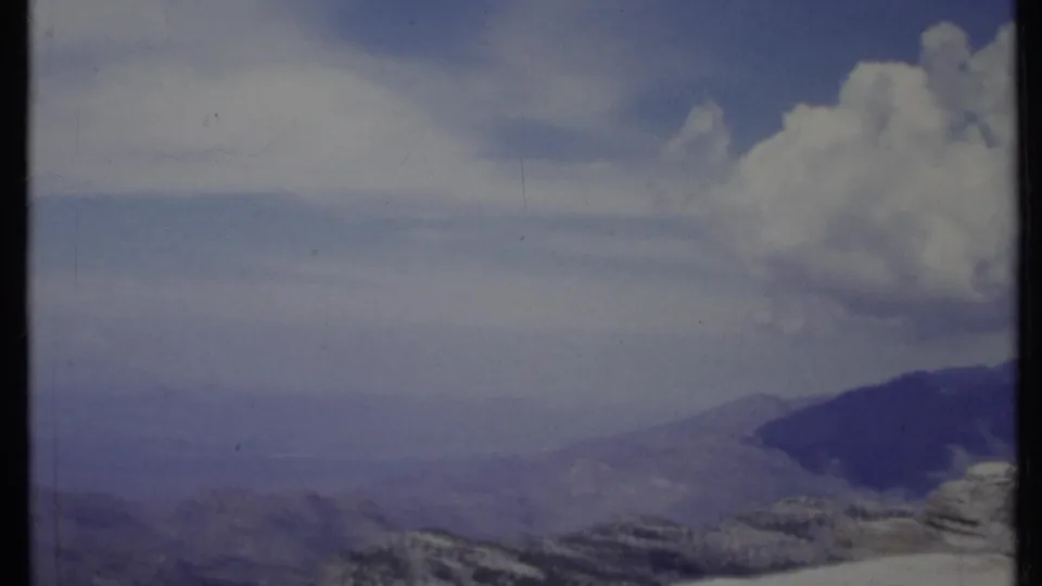 1971 California 8mm frame with distant ridges, atmospheric haze, pale blue sky, and a prominent puffy cloud on the right.