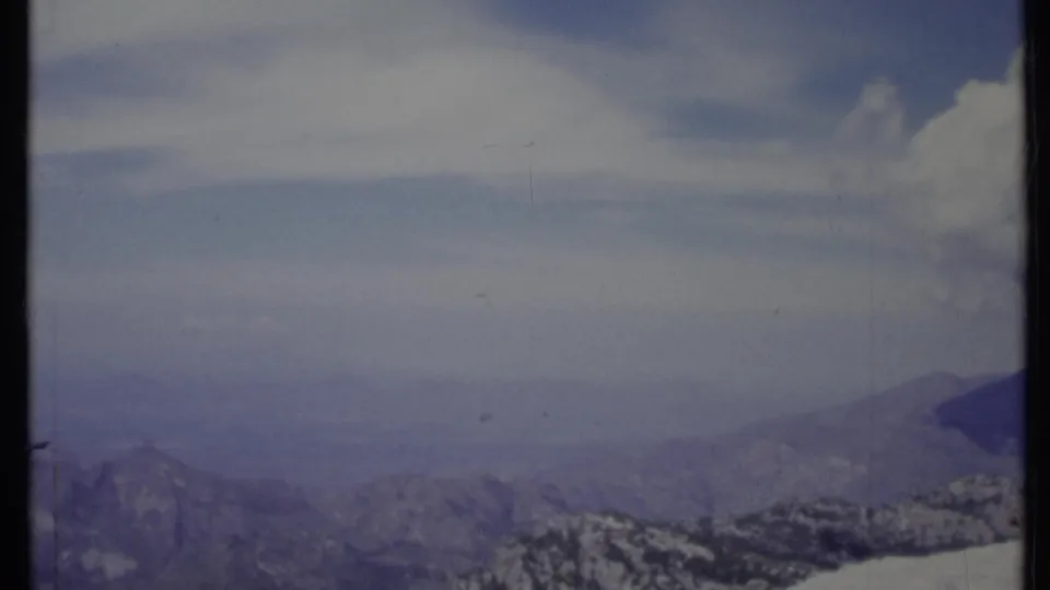 1971 California 8mm frame showing a hazy mountain panorama with muted blue tones, low ridges, and a bright cloud mass.