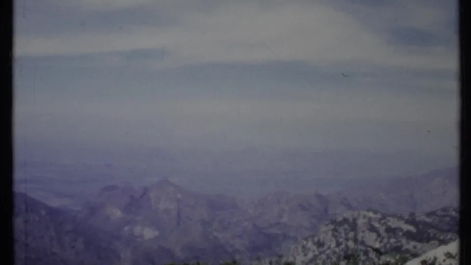 1971 California 8mm frame of layered mountain ridges and rocky terrain fading into a pale, hazy blue sky.