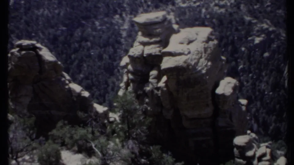 1971 California 8mm frame with sunlit sandstone-like rock spires standing above a dark green forested slope.