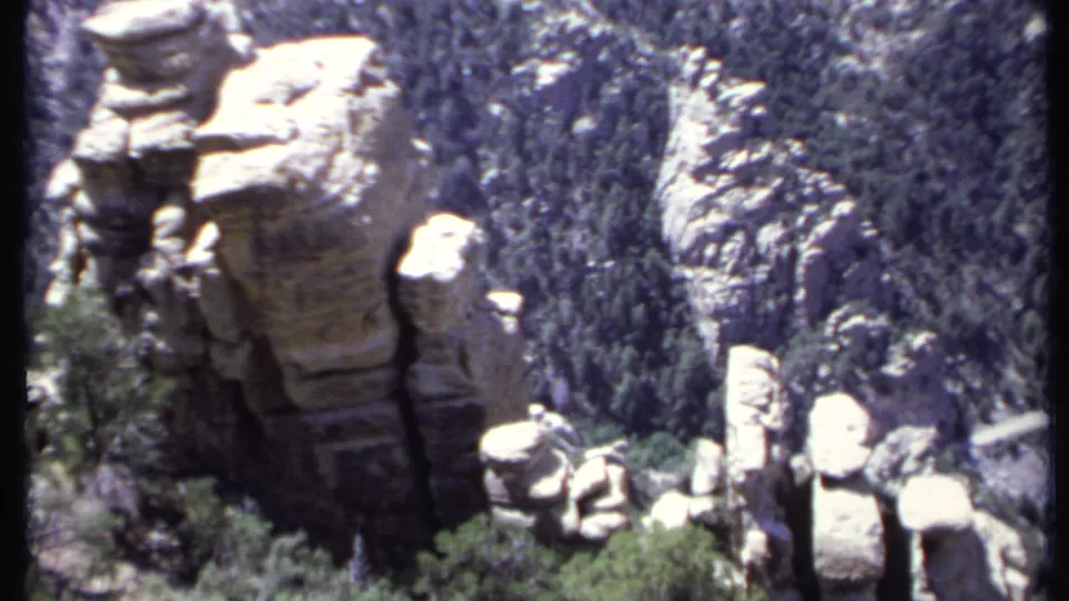 1971 California 8mm frame with multiple sunlit rock pillars, dense green forest, and steep rocky slopes in the background.