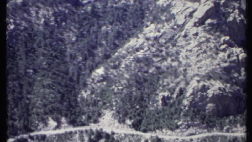 1971 California 8mm frame with a closer view of the mountain road, forest, and exposed rocky hillside.