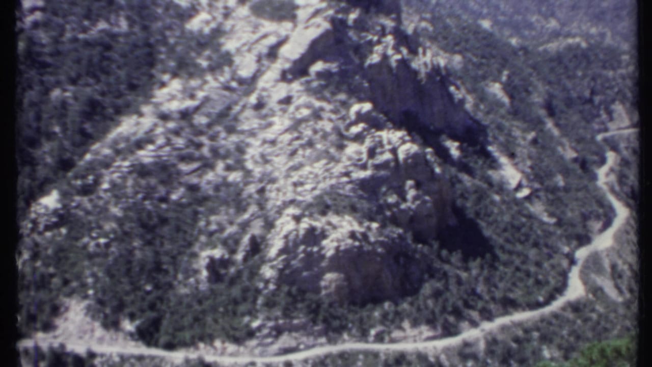 1971 California 8mm aerial frame showing rugged mountain slopes, patchy snow, and a road curving through the valley below.