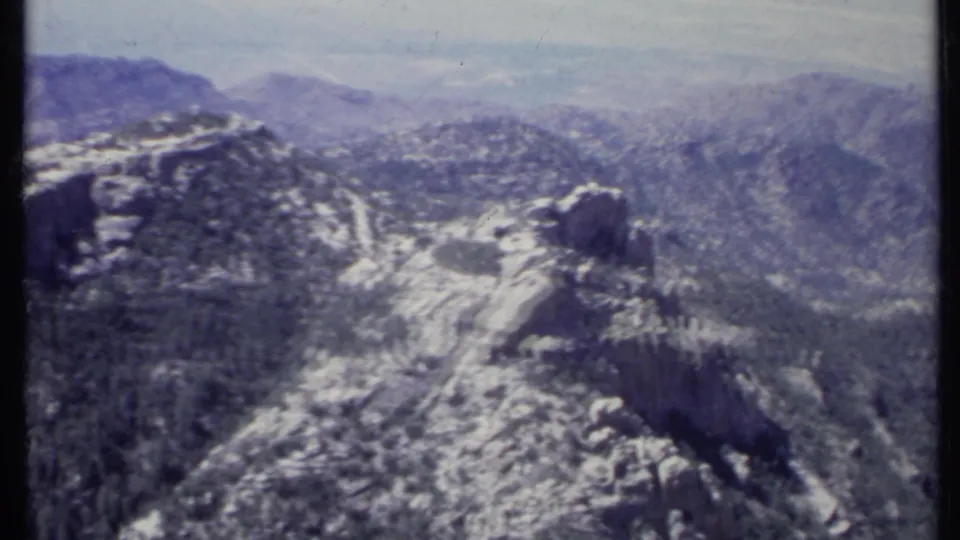 1971 California home-movie frame looking across rugged snowy mountain terrain toward layered peaks under a pale sky.