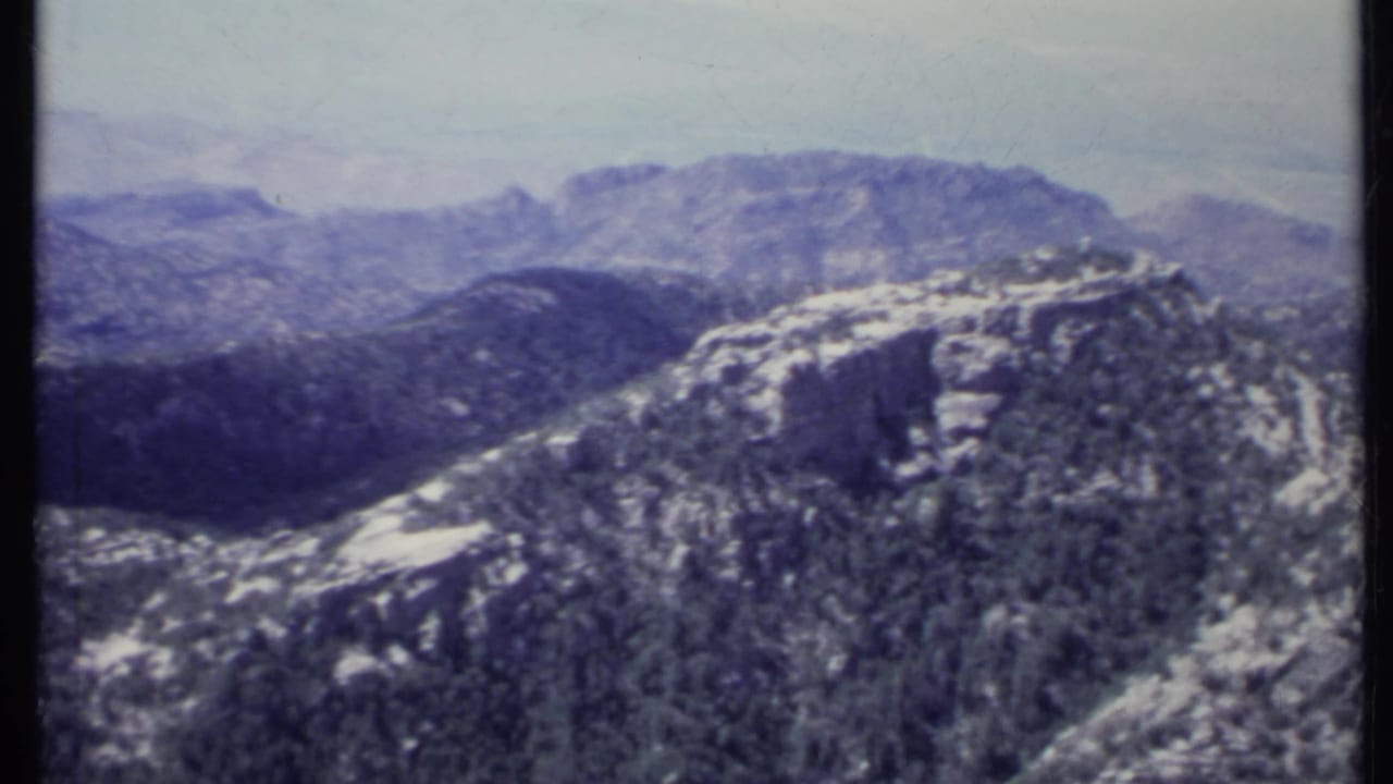 Rocky mountain ridge with sparse trees and hazy distant peaks.