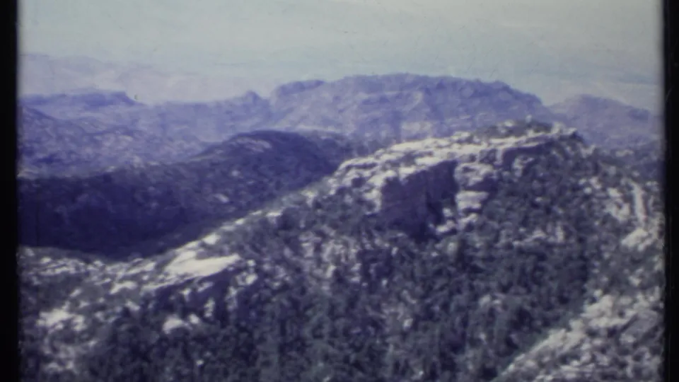 1971 California 8mm view of rugged mountain ridges with sparse trees, pale rock, and hazy distant highlands.