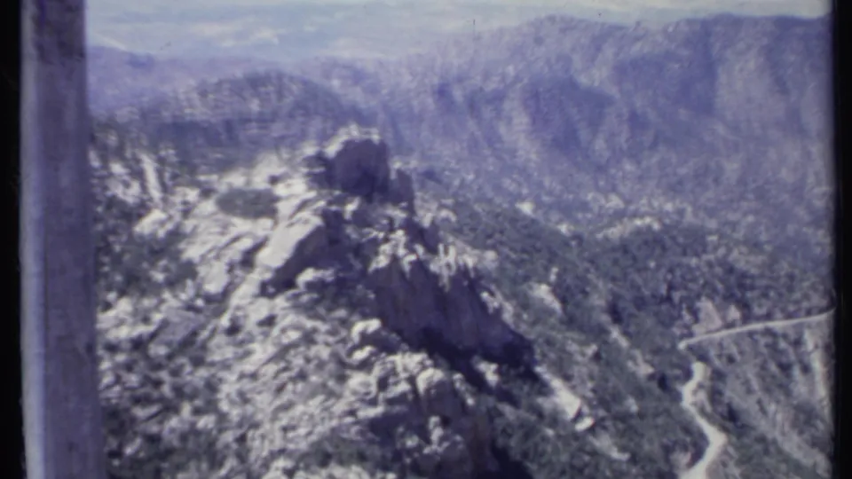 1971 California 8mm view over rocky mountain terrain, scattered vegetation, and a road tracing the lower slope.