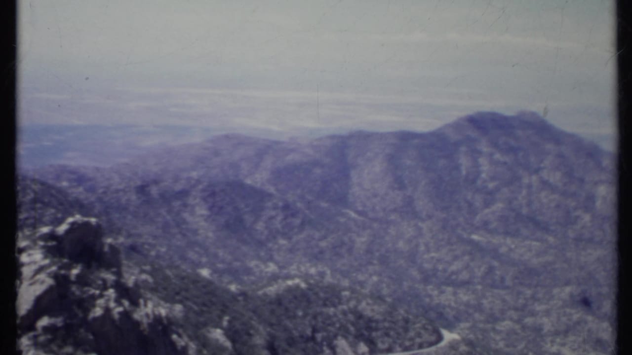 Hazy mountain ridge with rocky foreground and forested slopes below.