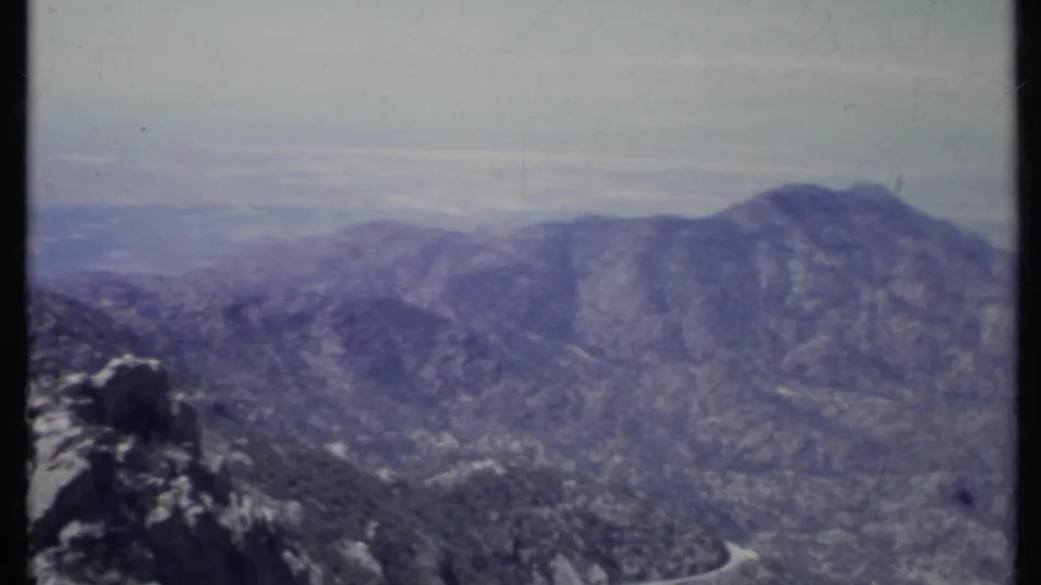 1971 California 8mm frame showing a hazy mountain ridge, rocky outcrop, and forested slopes in soft blue-purple film color.