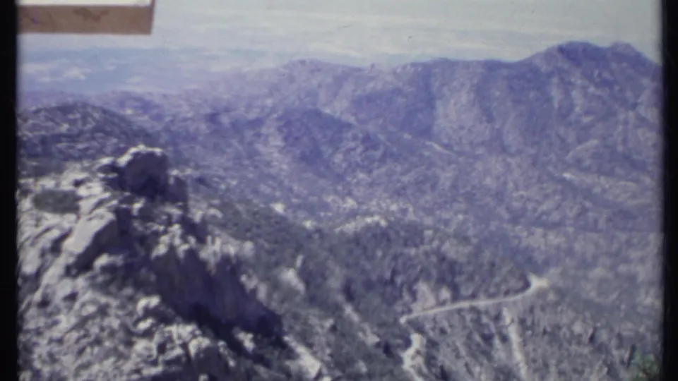 1971 California 8mm frame with a large rock formation in the foreground and a winding road across faded mountain hillsides.