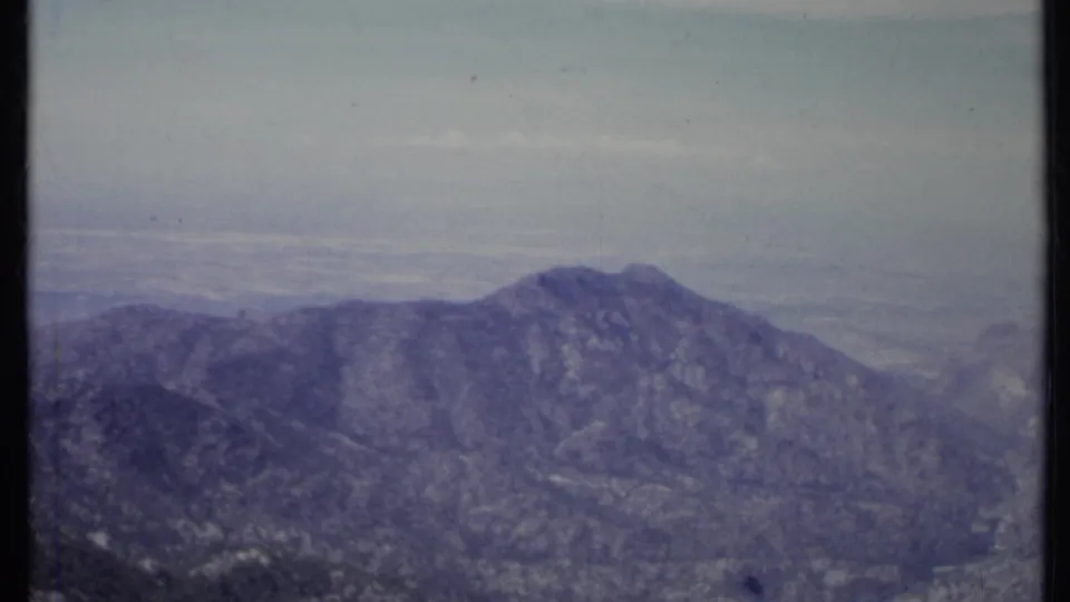 1971 California 8mm frame showing a rugged mountain ridge beneath a hazy pale sky, with soft focus and aged color cast.
