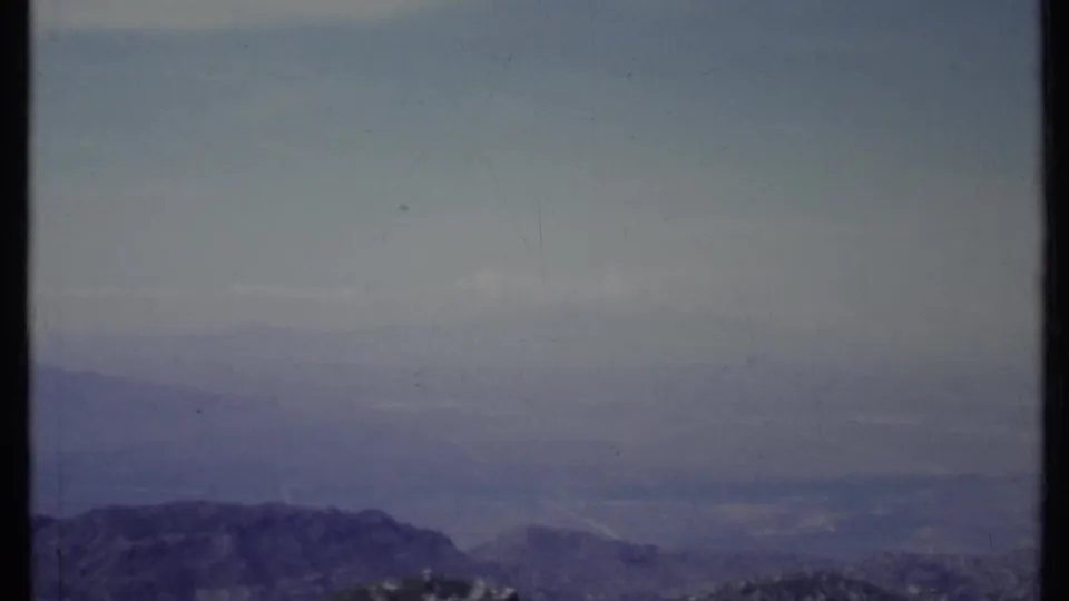 1971 California 8mm frame looking from a mountain slope toward a distant valley softened by haze and faded film color.